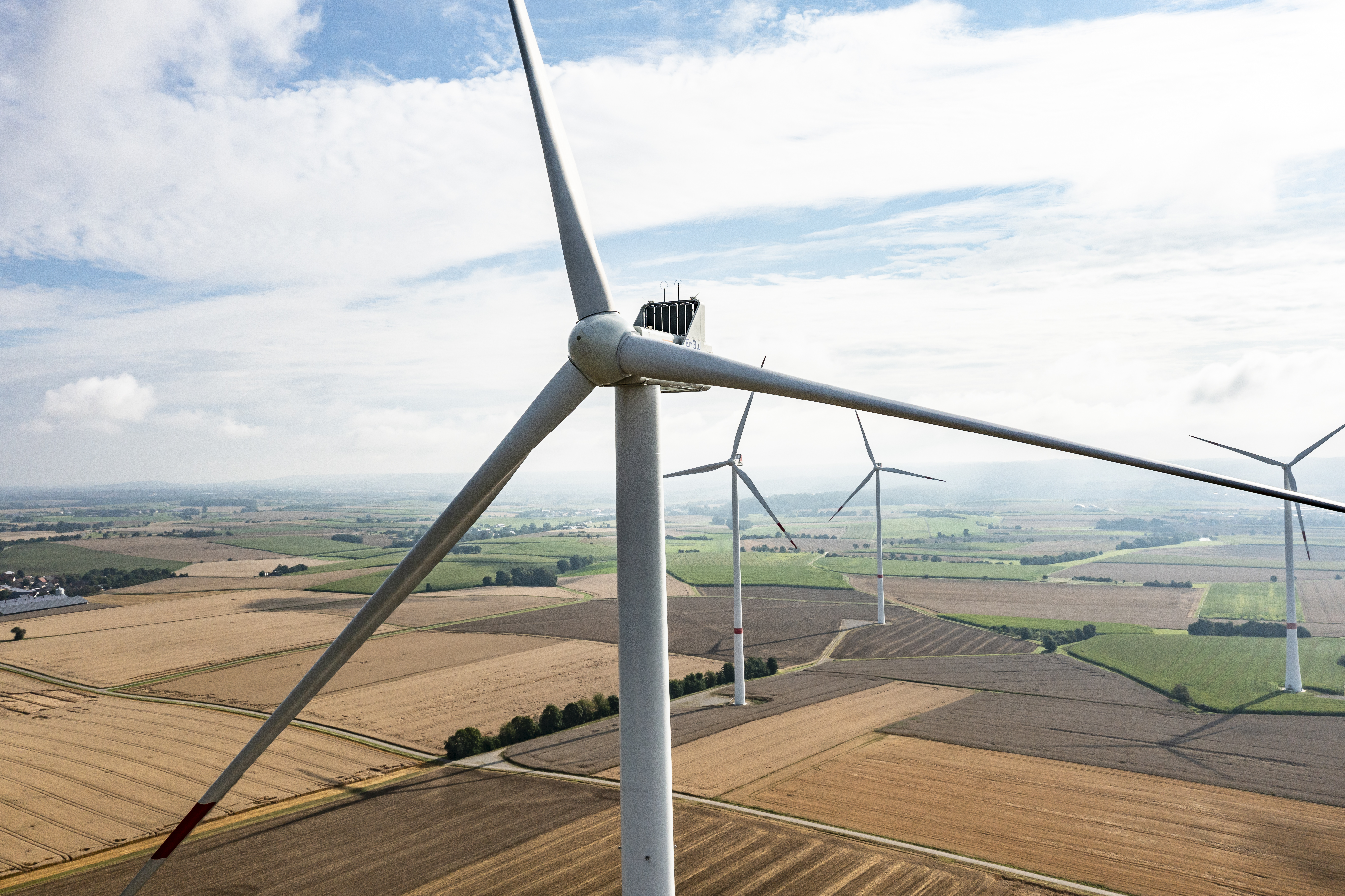 Vier Windräder bei bewölktem Himmel. Ein Windrad ist im Vordergrund mit den Rotorblättern fokussiert.