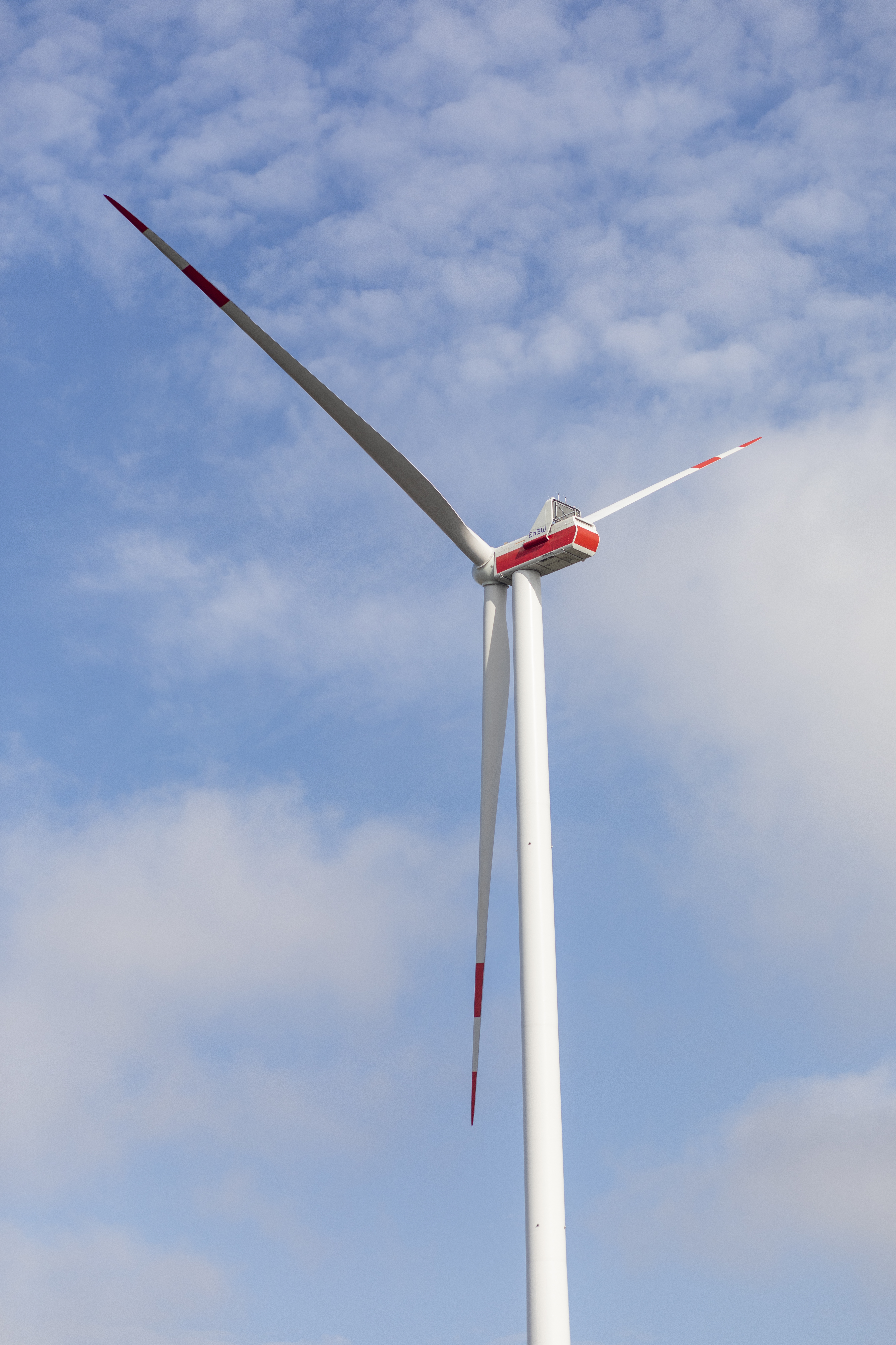 Ein Windradmast mit Rotorblättern bei leicht bewölktem Himmel mit Perspektive vom Boden aus.