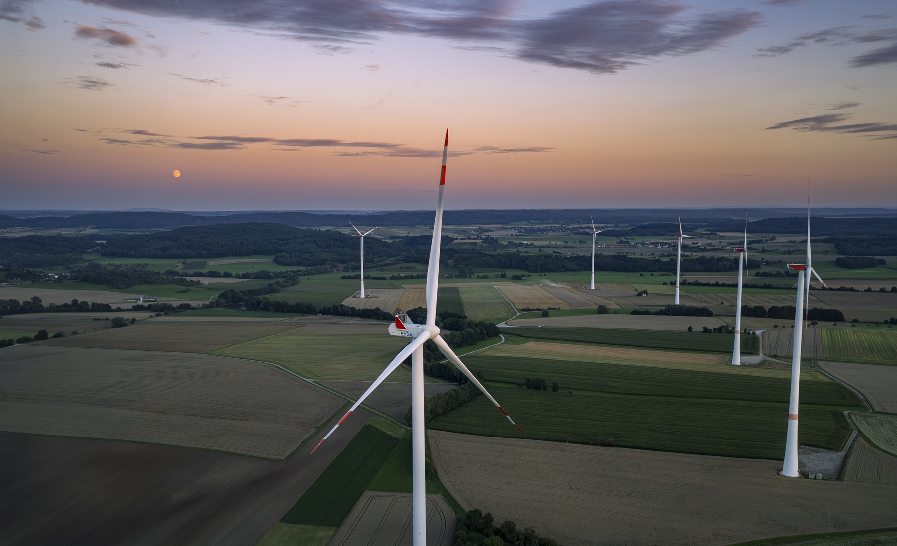Ein Windpark mit fünf Windrädern bei Sonnenuntergang in einer grünen Wiesenlandschaft.