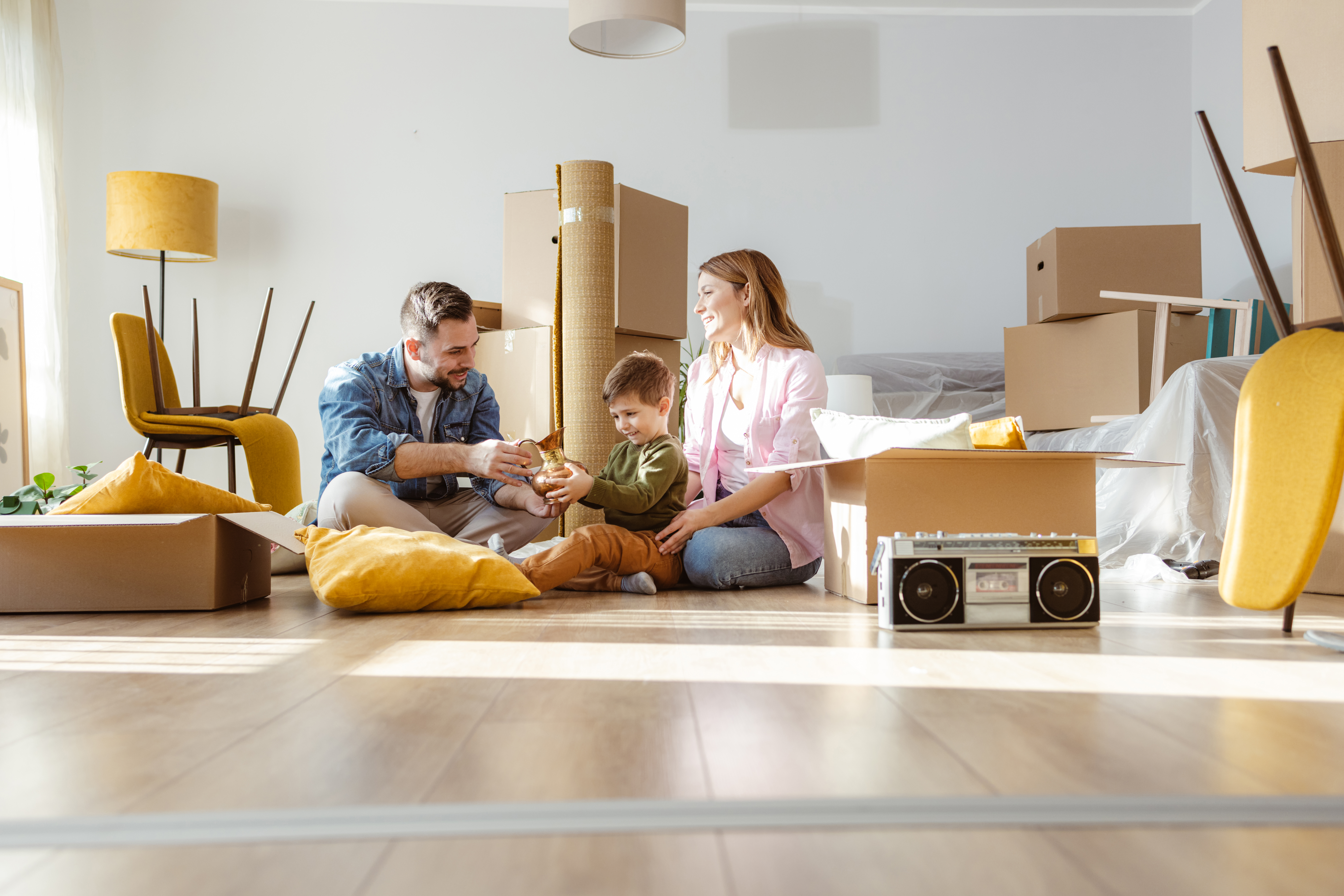 Eine junge Familie sitzt in ihrer neuen Wohnung umgeben von Umzugskartons