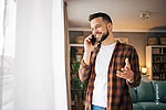 Ein Kunde telefoniert zuhause im Wohnzimmer mit dem Smartphone und lächelt abei.