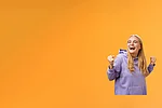 Eine Kundin freut sich sehr über den Gewinn des Treuegewinnspiels der EnBW ODR AG. Sie trägt einen lila Pullover vor orangenem Hintergrund.