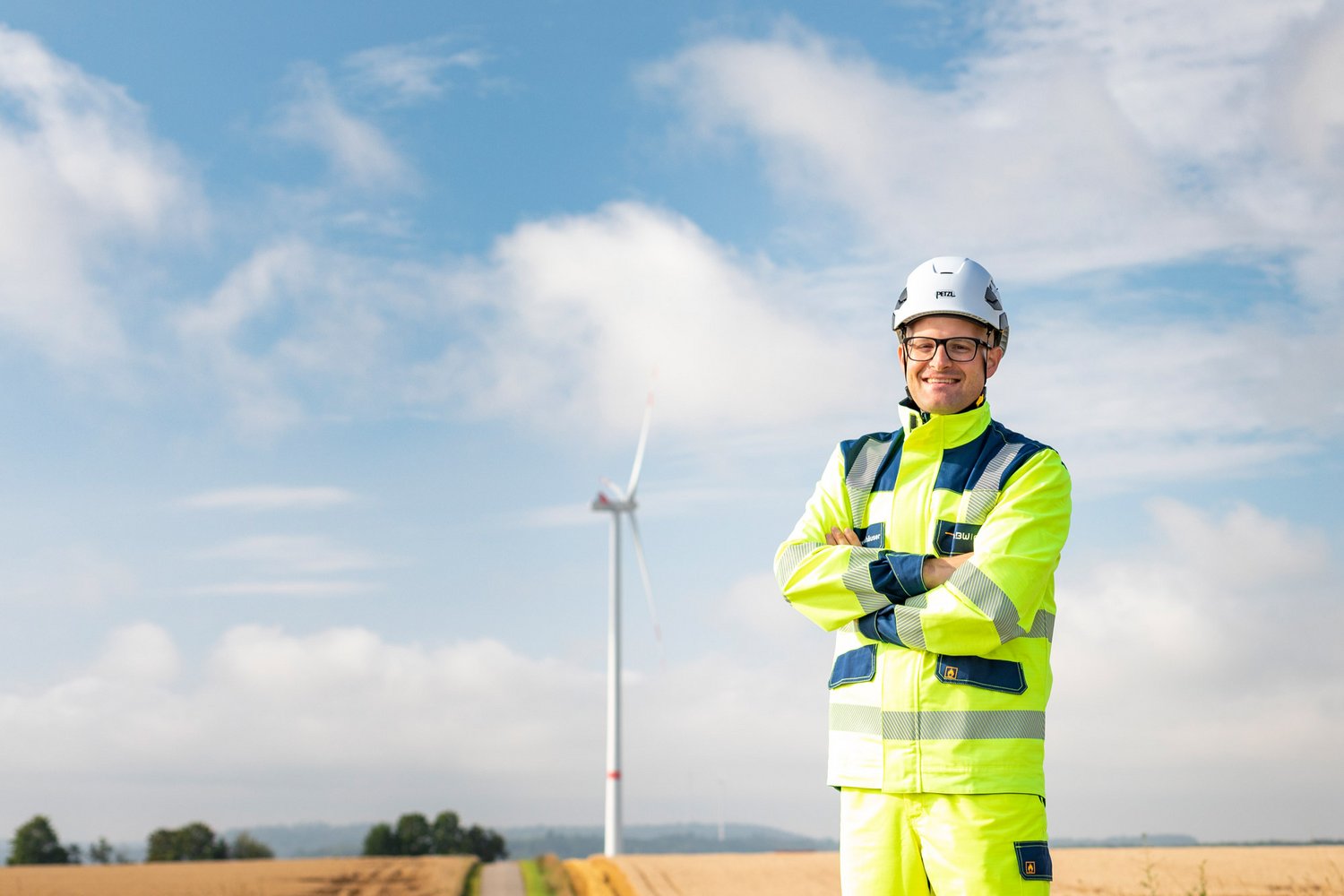 Mann mit EnBW ODR Arbeitsanzug steht auf einem Feld vor einem Windrad