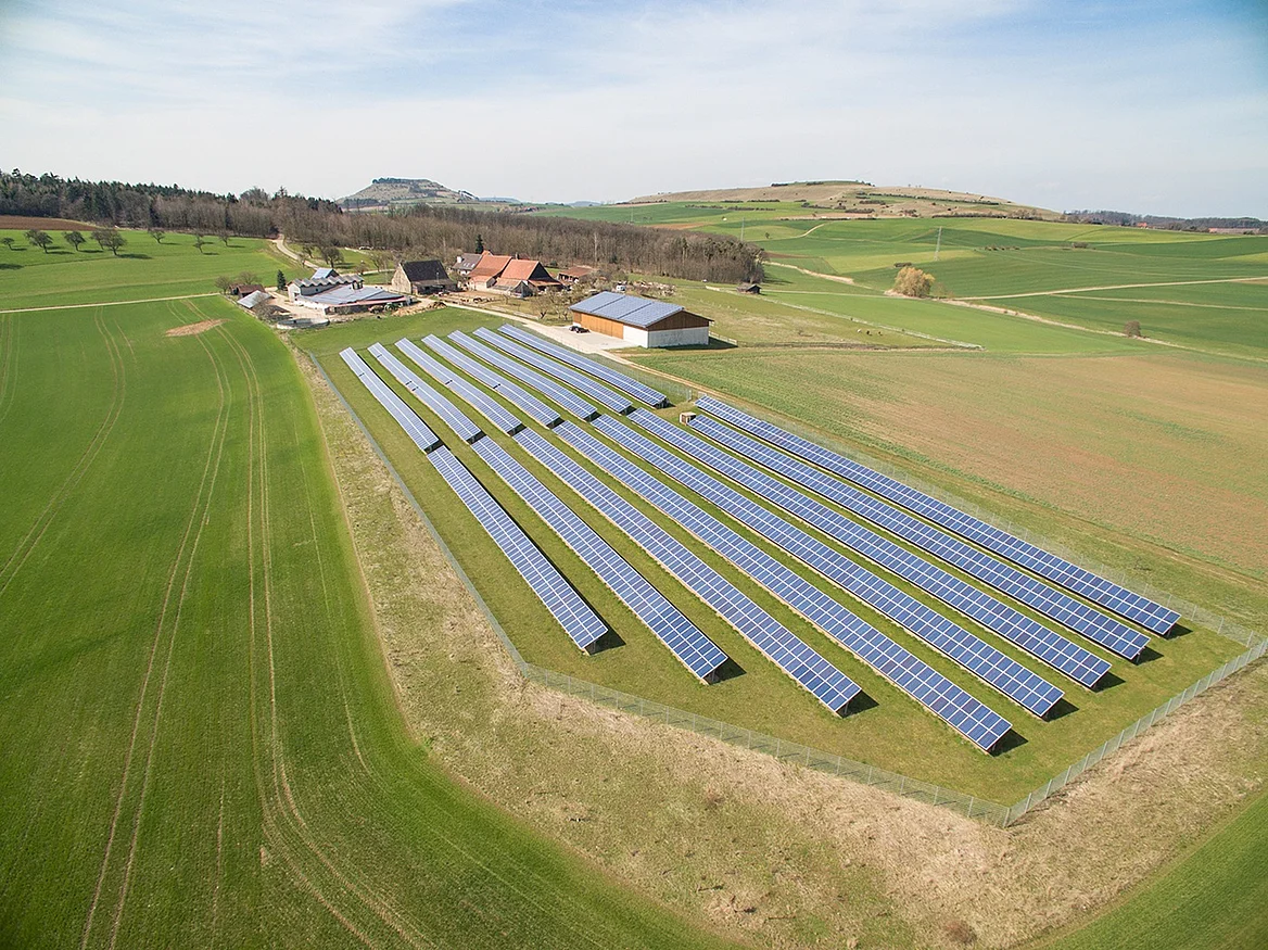 Viele Photovoltaikanlagen stehen auf einem freien Feld neben einem Bauernhof