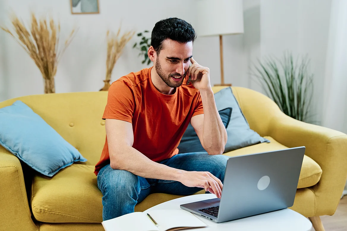 Ein Kunde telefoniert zu Hause vor dem Laptop auf dem Sofa