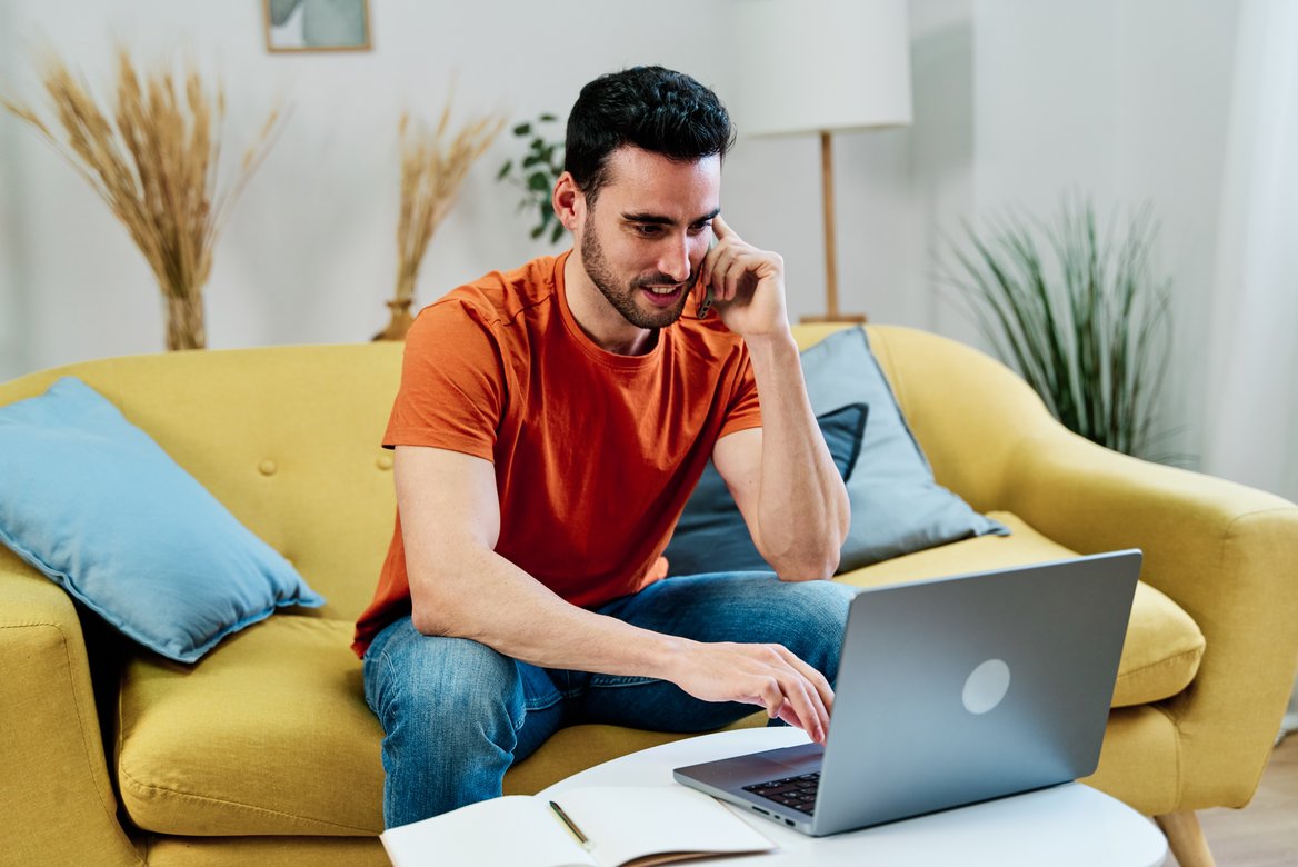 Ein Kunde telefoniert zu Hause vor dem Laptop auf dem Sofa