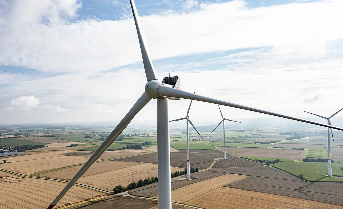 Vier Windräder bei bewölktem Himmel. Ein Windrad ist im Vordergrund mit den Rotorblättern fokussiert.