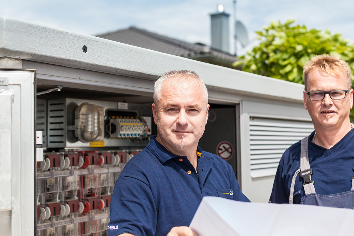 Zwei Mitarbeiter mit einem Schaltplan vor einem Verteilerkasten