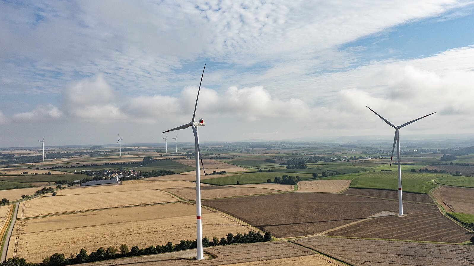 Zwei Windräder auf einem Feld bei Sonnenschein.