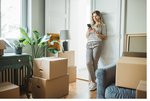 Eine Kundin lehnt zu Hause an der Wand ihrer neuen Wohnung umgeben von Umzugskartons und informiert sich über ihr Smartphone.