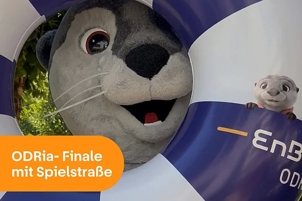 ODRia-Finale mit Spielstraße: Das Maskottchen der EnBW ODR, ODRi der Otter, schaut fröhlich durch einen großen Schwimmreifen mit dem Logo-Aufdruck der EnBW ODR AG.