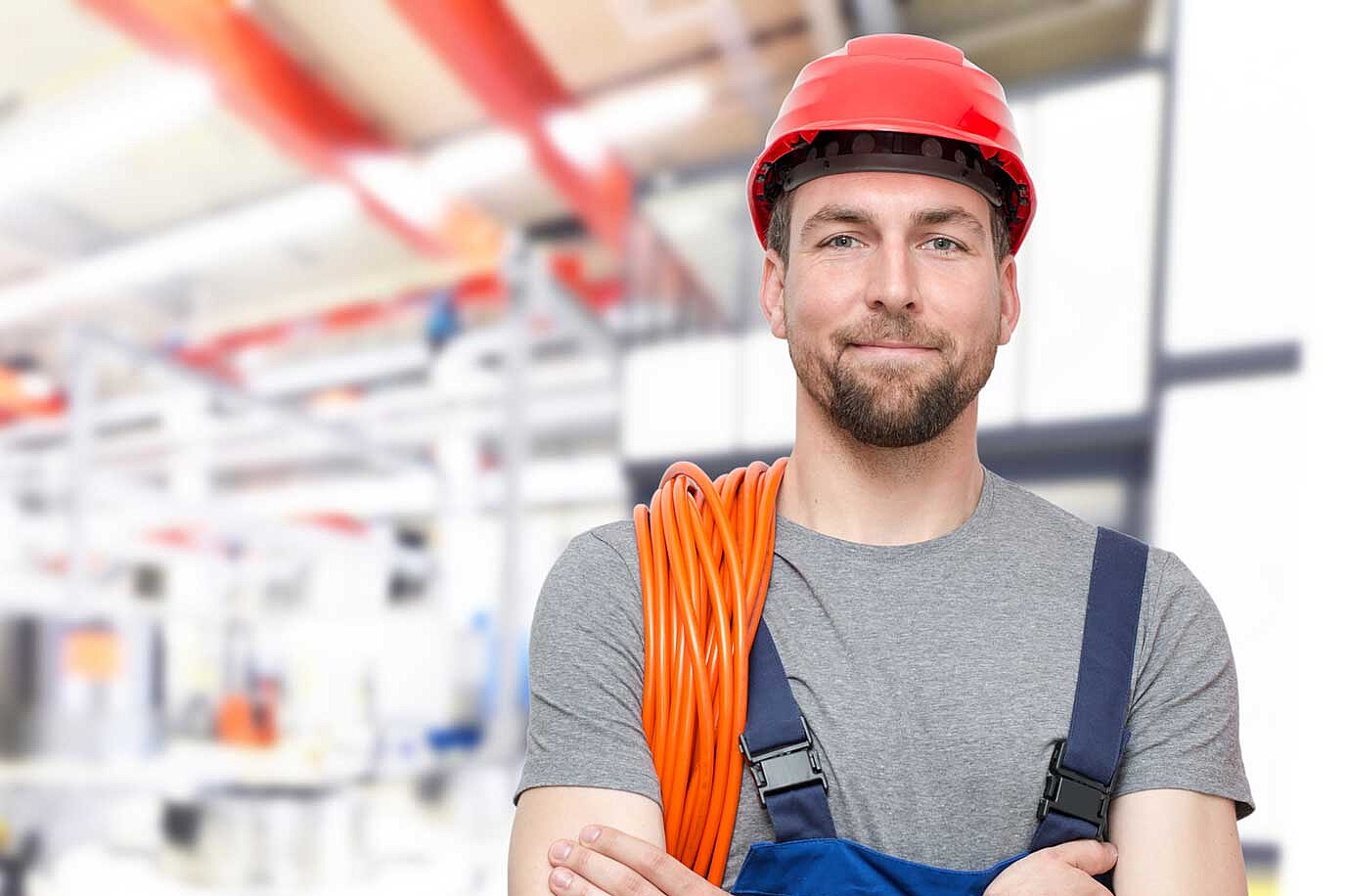 Mann in Arbeitskleidung, rotem Helm und orangenem Kabel über der Schulter