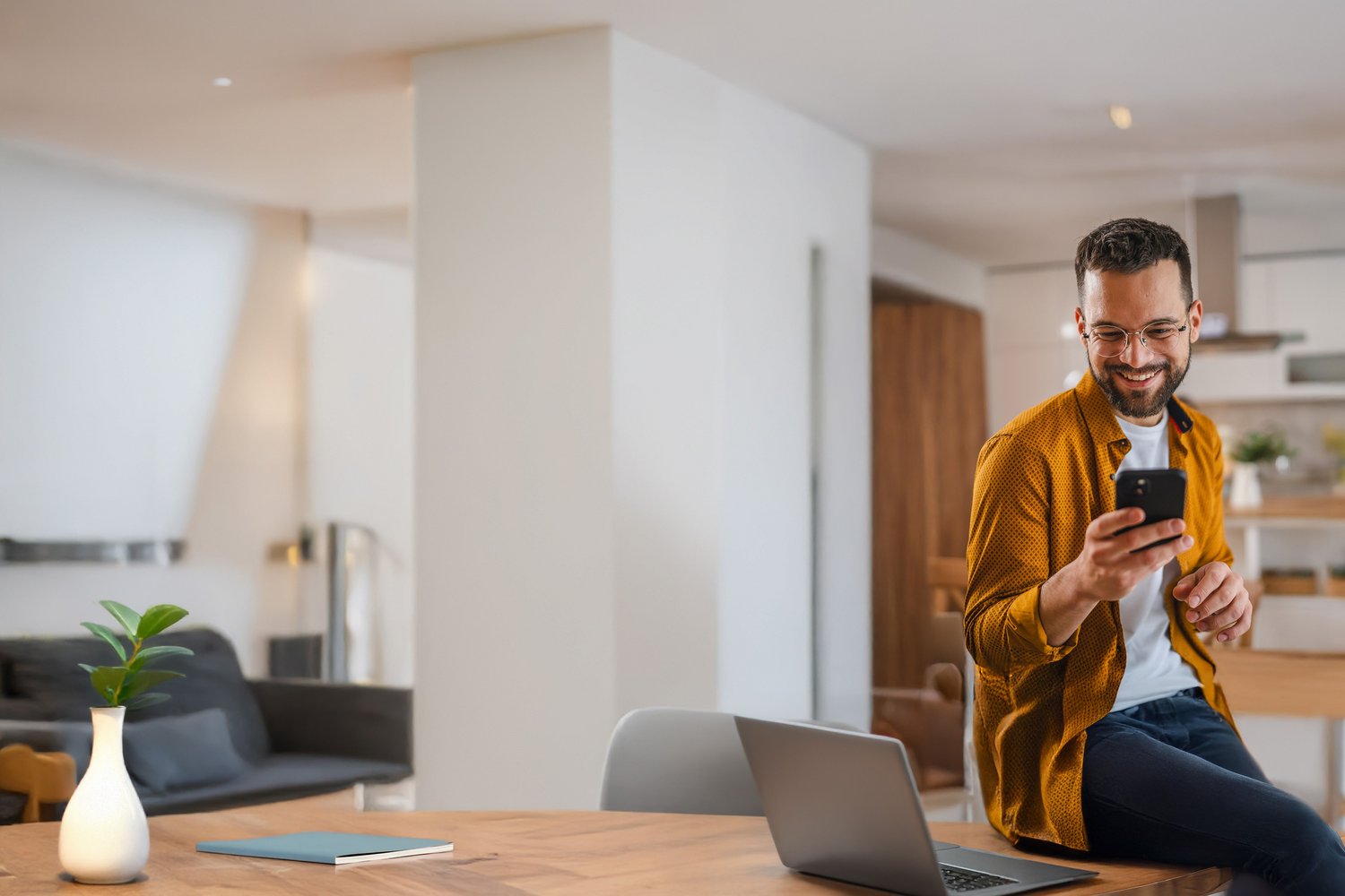 Ein Kunde zuhause am Esstisch schaut in sein Smartphone und freut sich