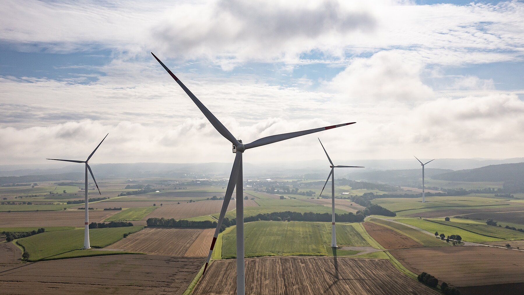 Vier Windräder bei bewölktem Himmel mit leichtem Sonnenschein.